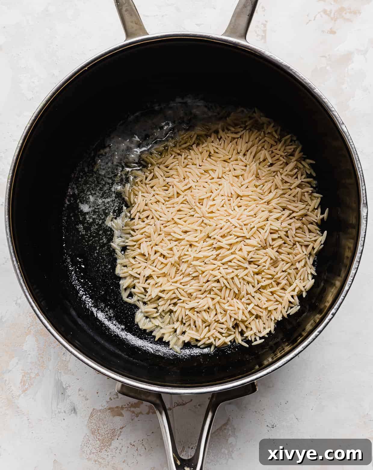 Orzo Pilaf 4 Orzo pasta gently toasting in melted butter within a black non-stick saucepan, beginning to acquire a golden hue.