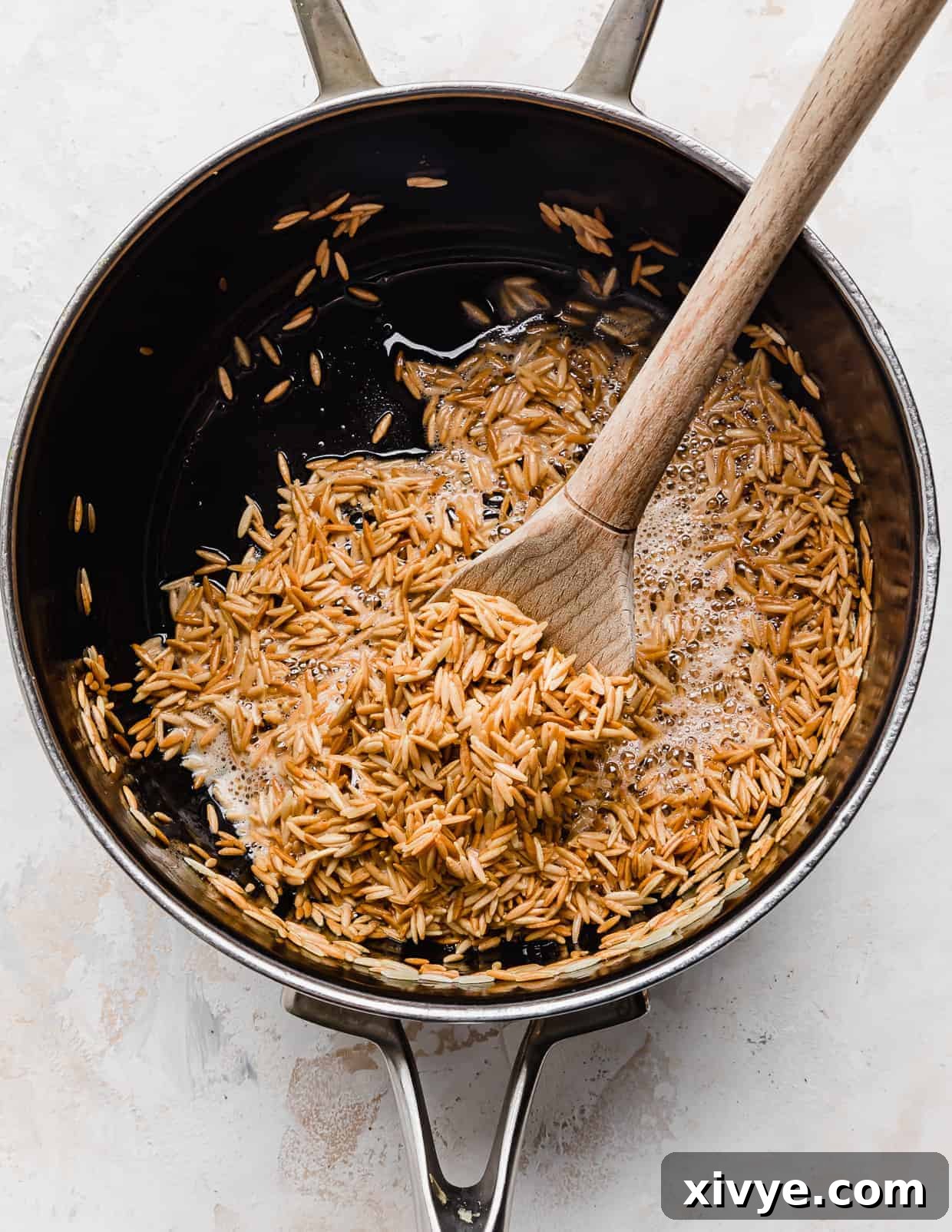 Orzo Pilaf 5 Perfectly golden brown orzo pasta shimmering in butter within a saucepan, indicating it's ready for the next step.