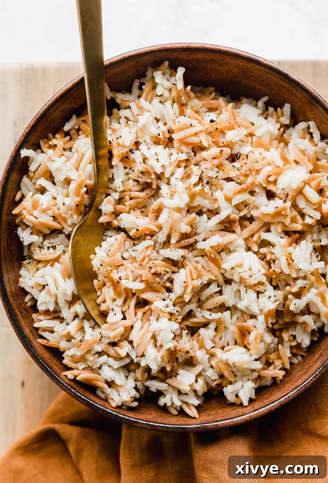 Orzo Pilaf 9 A elegant golden spoon is poised in a large, inviting brown bowl filled with warm, fluffy Orzo Rice Pilaf, ready to be enjoyed.