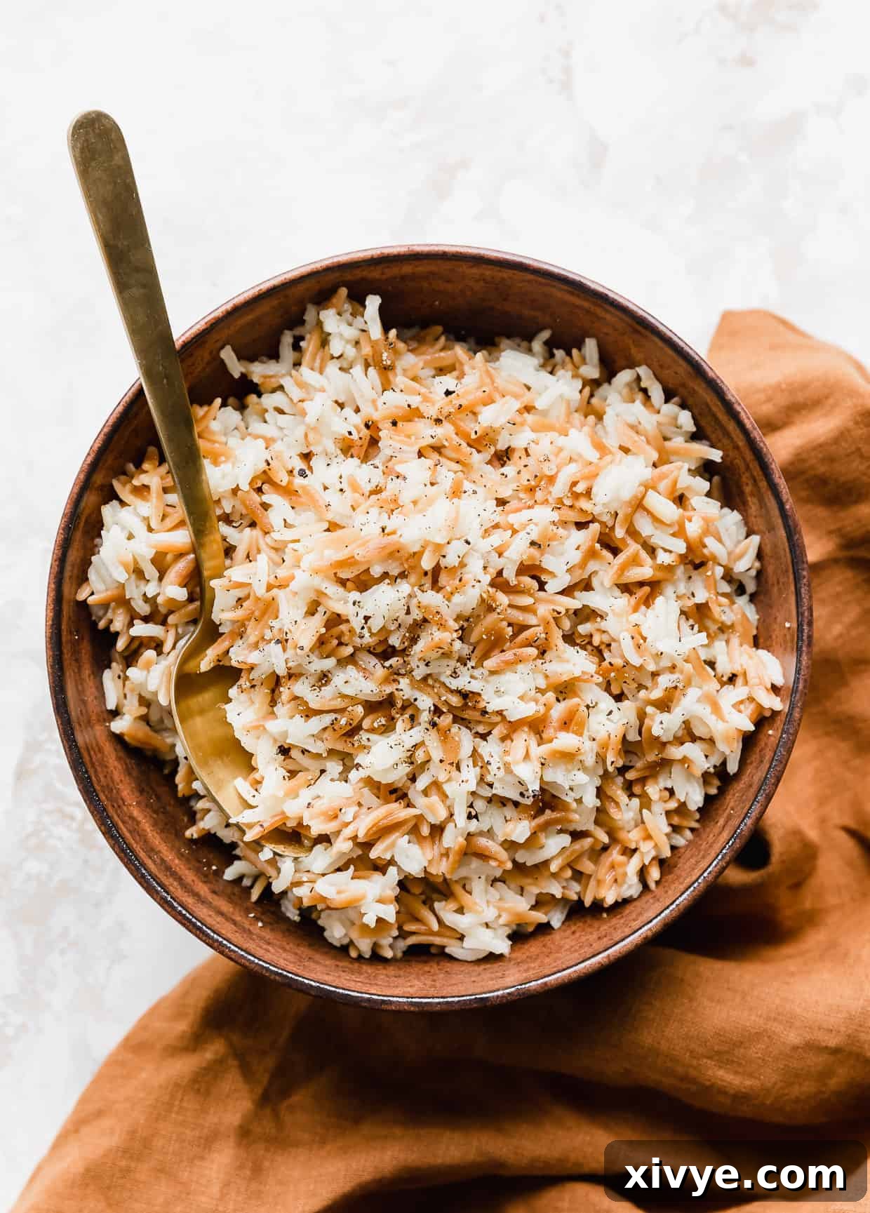 Orzo Pilaf 10 A close-up shot of the Orzo Rice Pilaf in a brown bowl, with a golden spoon resting inside, showcasing its fluffy texture and golden hue.