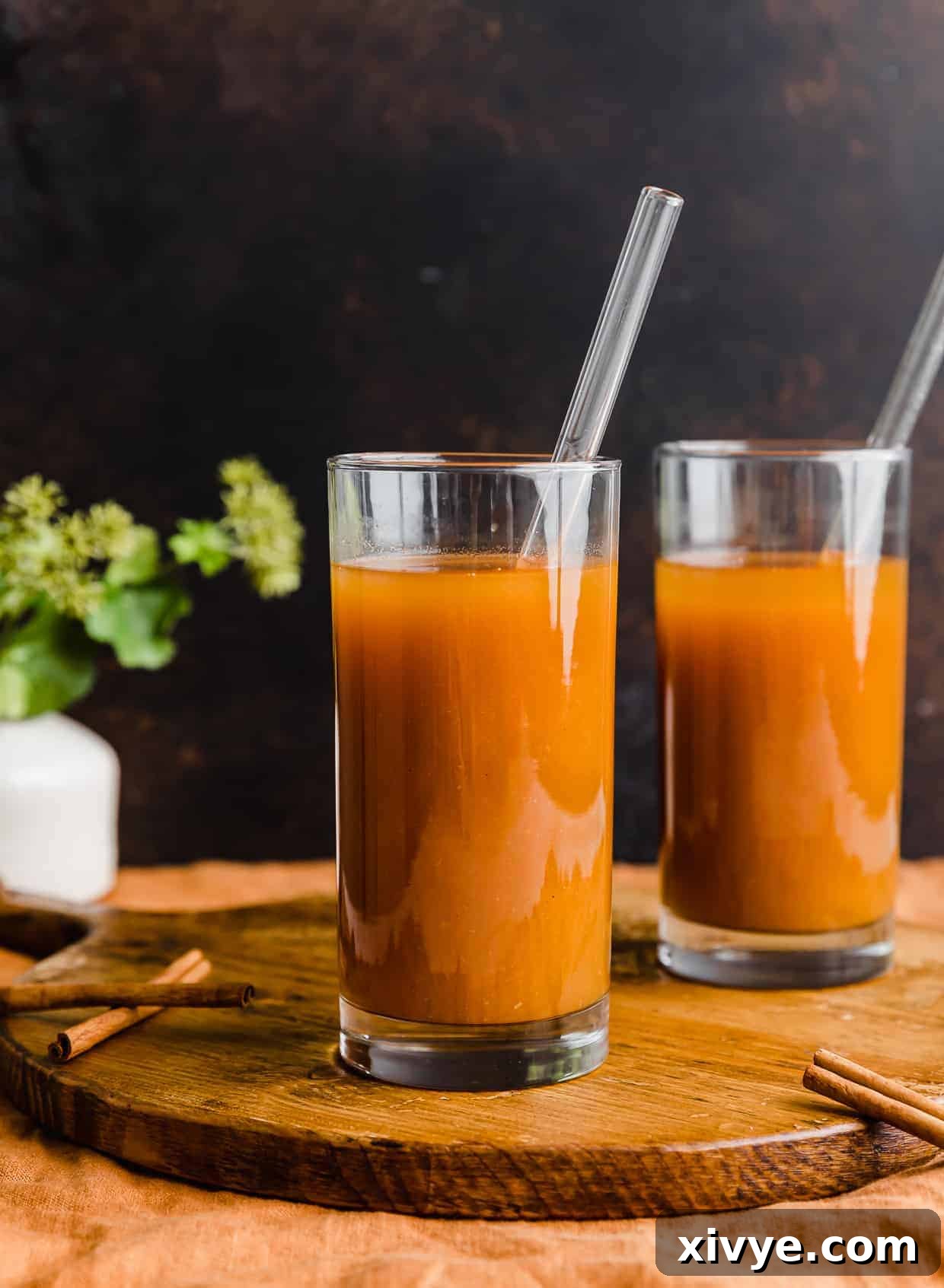 Two glasses with orange pumpkin juice in them against a brown background.