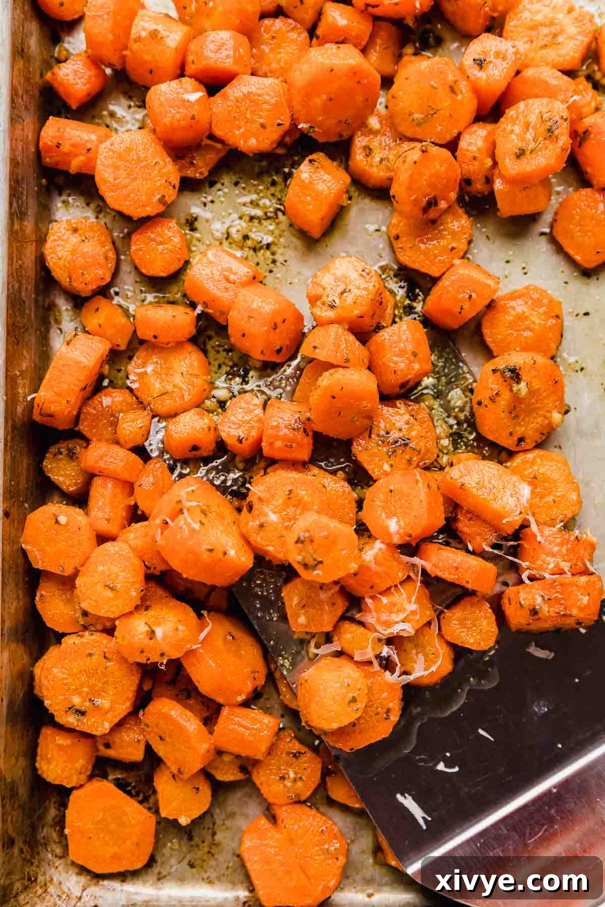 Perfectly sliced Garlic Butter Roasted Carrots, glistening with melted butter and sprinkled with fresh herbs, ready for serving on a baking sheet.