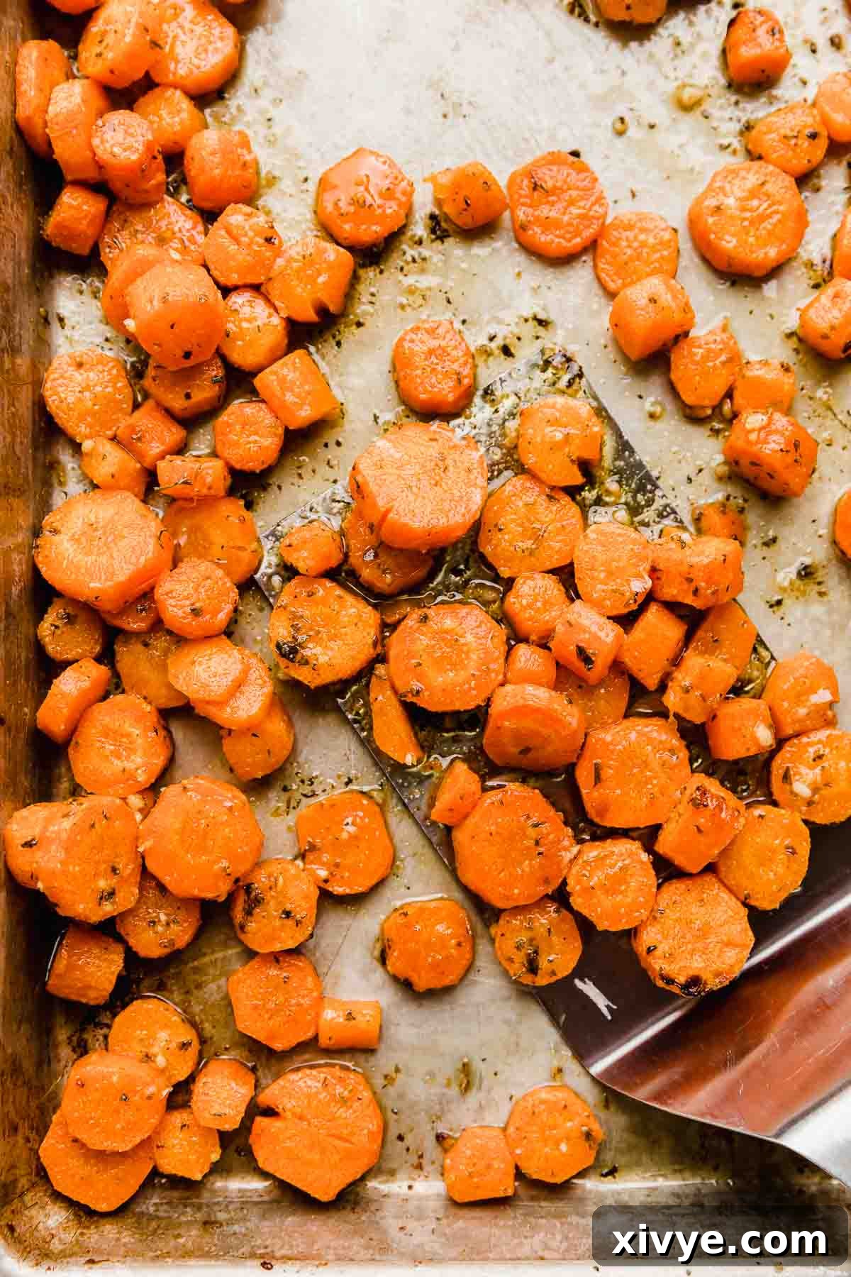 Garlic parmesan roasted carrots, perfectly sliced into coins and spread in a single layer on a baking sheet, showcasing their golden-brown edges and vibrant color.