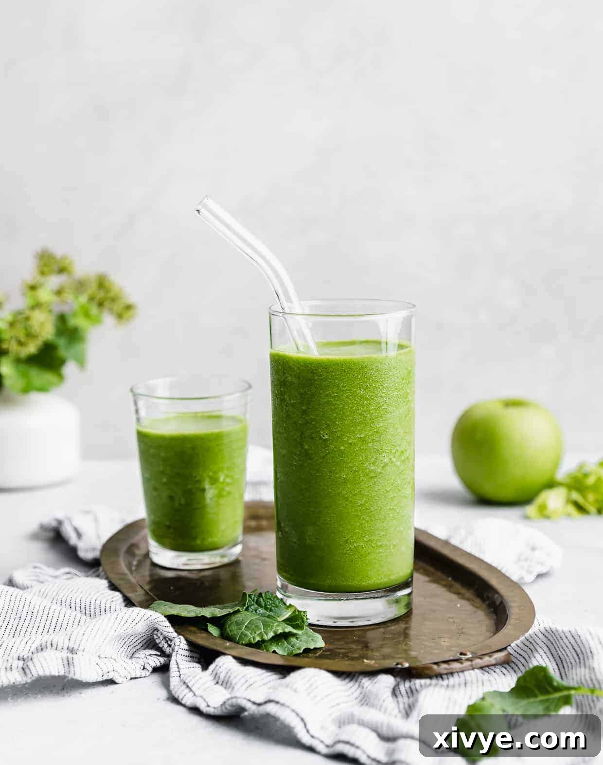 A clear glass full of bright green celery smoothie with a glass straw in the cup. 