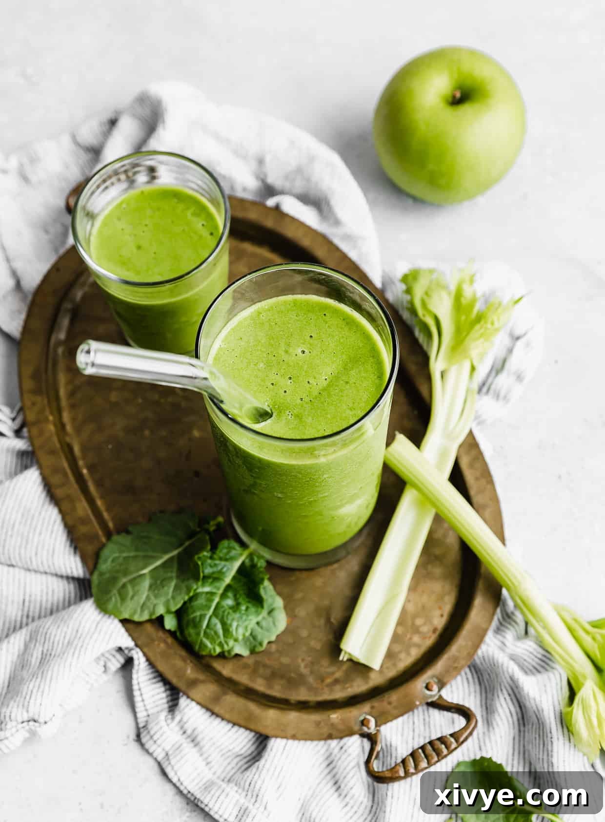 A celery smoothie in a glass cup with a glass straw in it. 