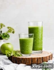 Two glasses full of dark green celery smoothie on a wooden round board.
