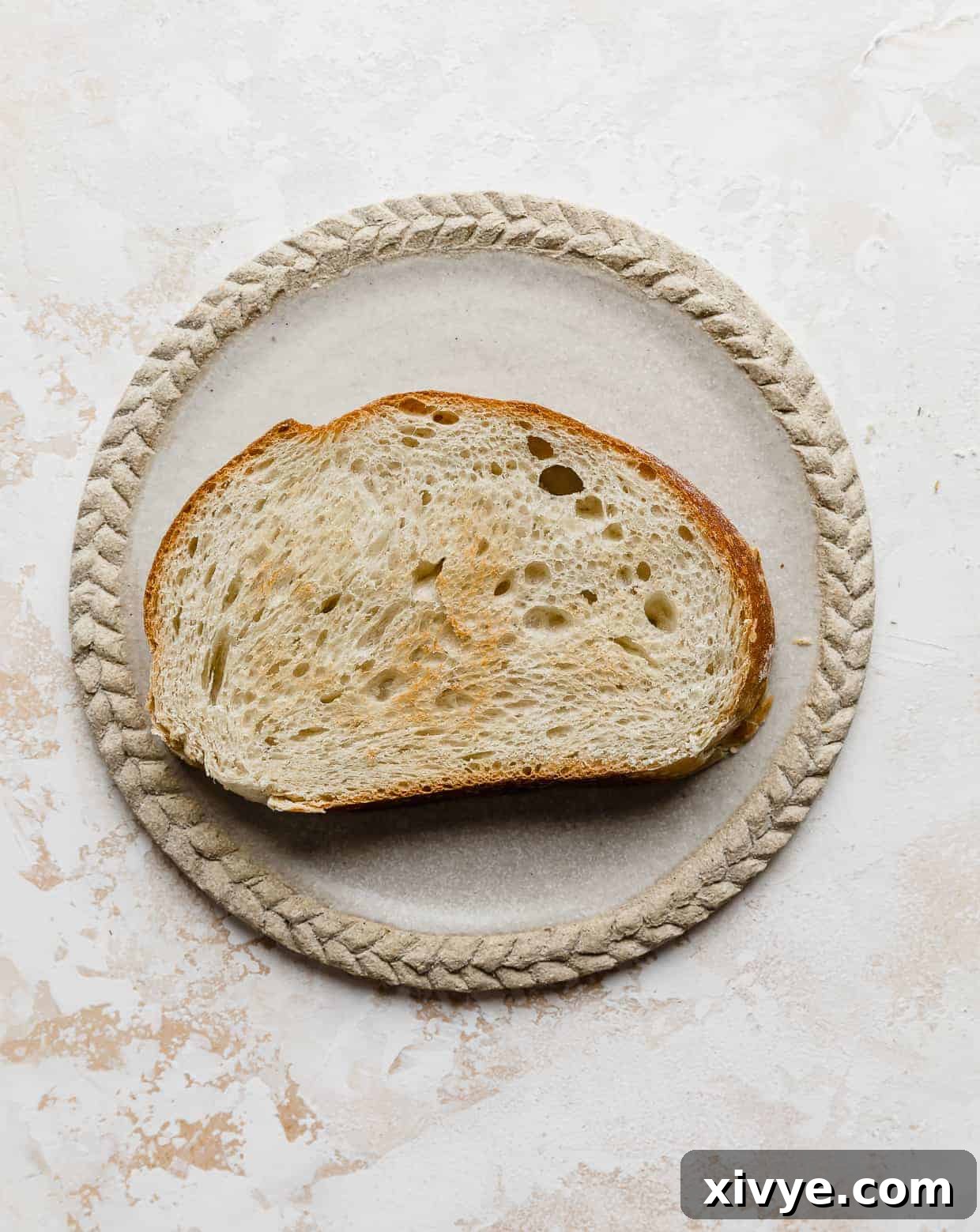 Creamy Avocado Egg Toast 4 Slice of toasted French bread on a tan plate, ready for toppings.
