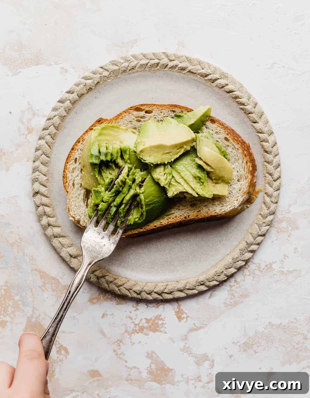 Creamy Avocado Egg Toast 5 A fork smashing fresh avocado on a slice of toasted bread, creating a creamy spread.