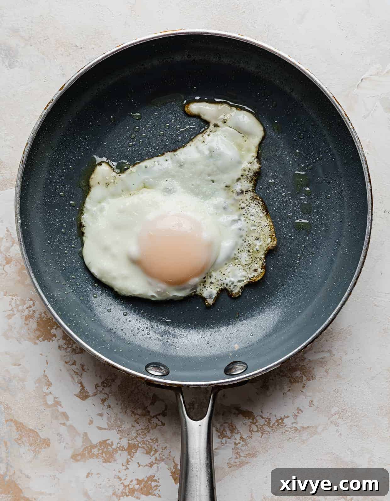 Creamy Avocado Egg Toast 7 A perfectly cooked sunny-side up egg in a gray skillet, ready to be transferred.