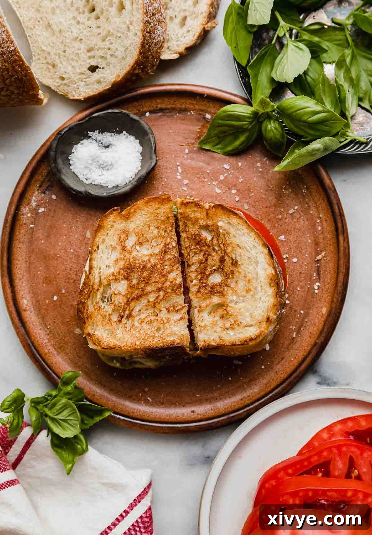 Artisan Pesto Mozzarella Sandwich 5 Pesto Mozzarella Sandwich on a brown plate, sliced in half with fresh basil in a bowl at the right corner of the photo, ready to be served.