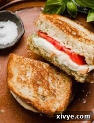 Pesto Mozzarella Sandwich on French bread, sliced in half with fresh tomatoes on the sandwich too.