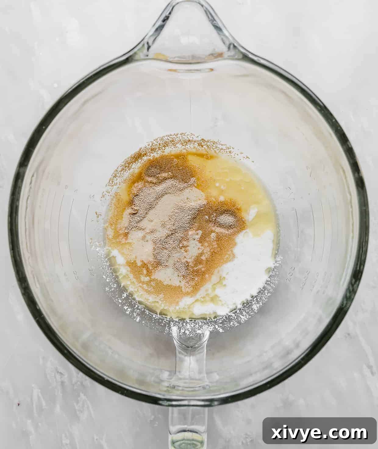 Irresistible Mini Cinnies 6 A glass stand mixer bowl containing warm water, buttermilk, sugar, melted butter, and yeast at the start of the dough making process.