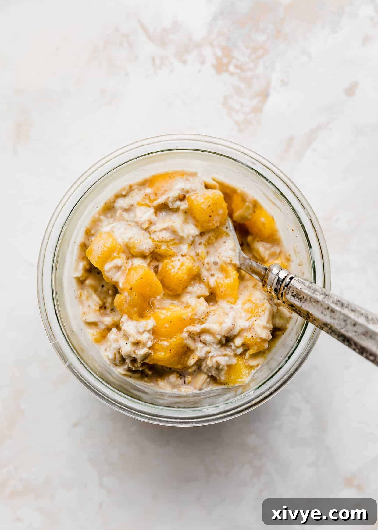 Overhead photo of a spoon scooping into mango overnight oats with cinnamon and nutmeg, highlighting the creamy texture and inviting aroma.