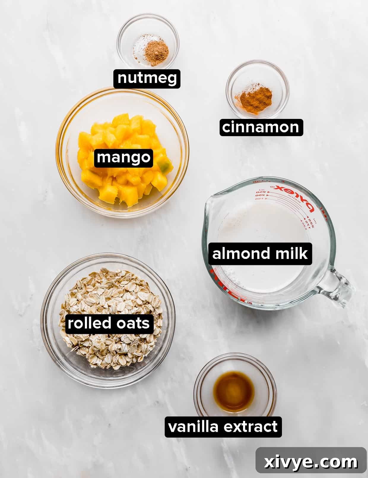 Ingredients used to make mango overnight oats, including rolled oats, diced mango, almond milk, and spices, arranged on a white background.