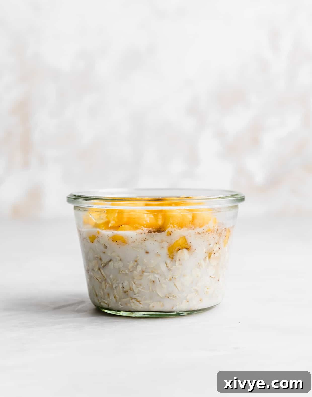 A glass jar with milk and oats on the bottom and diced mangos overtop, illustrating the layering process.