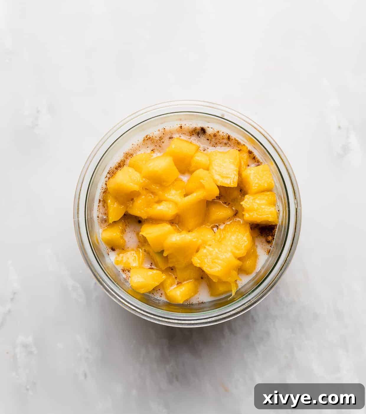 Diced mango overtop of a milk and oat mixture in a glass jar, perfectly demonstrating the serving suggestion.