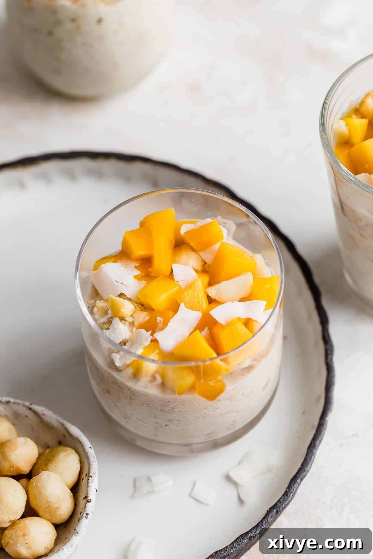 Diced mangos overtop of a Mango overnight oat mixture in a glass cup, ready to be enjoyed.