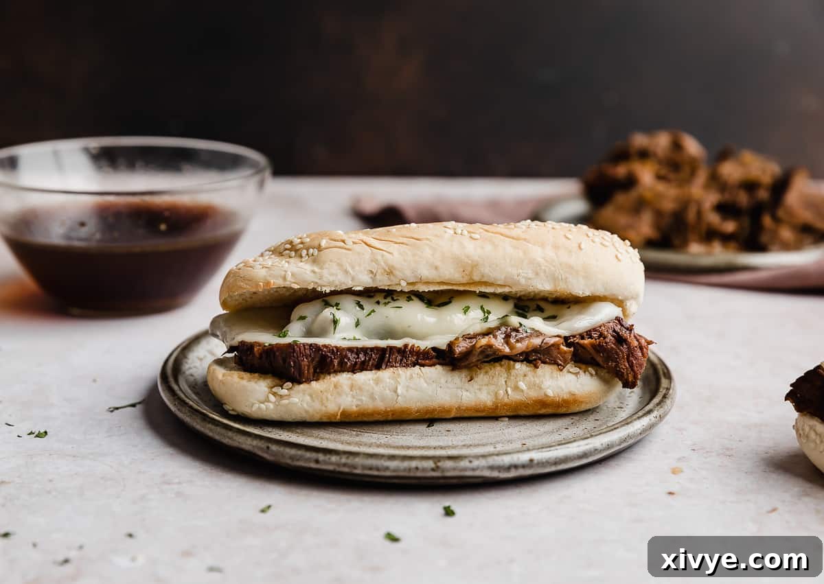 Ultimate Slow Cooker French Dip 8 A hoagie bun topped with tender crock pot French dip meat and provolone cheese, showcasing the melted cheese and juicy beef.