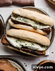 Two Slow Cooker French Dip Sandwiches topped with melty provolone cheese on a gray plate.