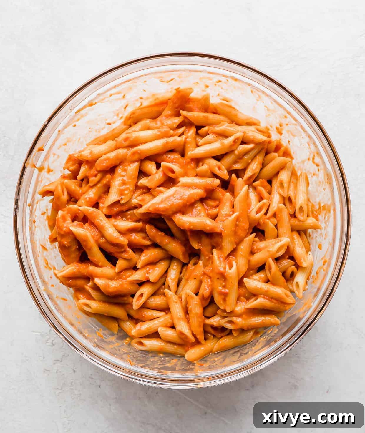 Cooked penne noodles tossed in a red sauce in a glass bowl.
