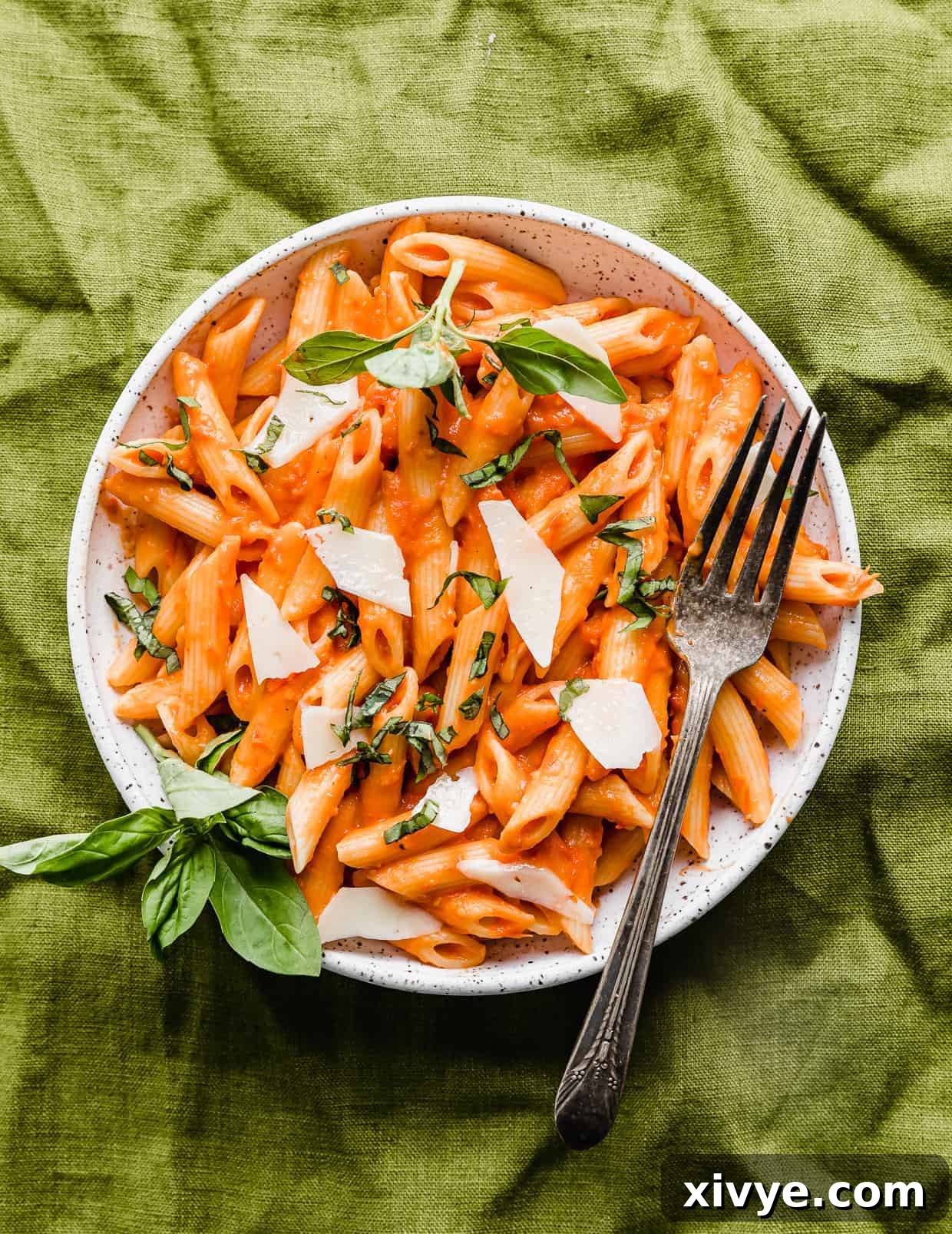 A white plate with Penne al Pomodoro on it, sitting on a green linen napkin.