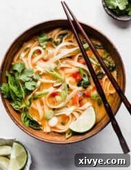 A bowl of Thai Red Curry Noodle Soup on a clean white background, showcasing its rich color and fresh garnishes.