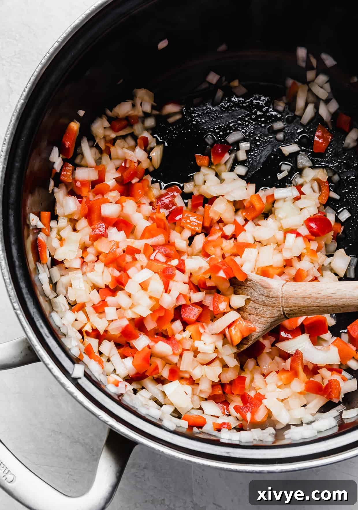 A black pot on a stove with diced onion and red bell pepper softening in olive oil, ready for the next step of Thai Red Curry Noodle Soup.