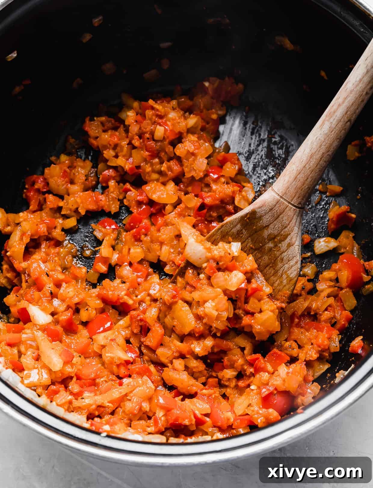 A close-up view of the sautéed diced onion and red bell pepper fully coated in red curry paste within a black pot, creating a rich and aromatic base for the soup.