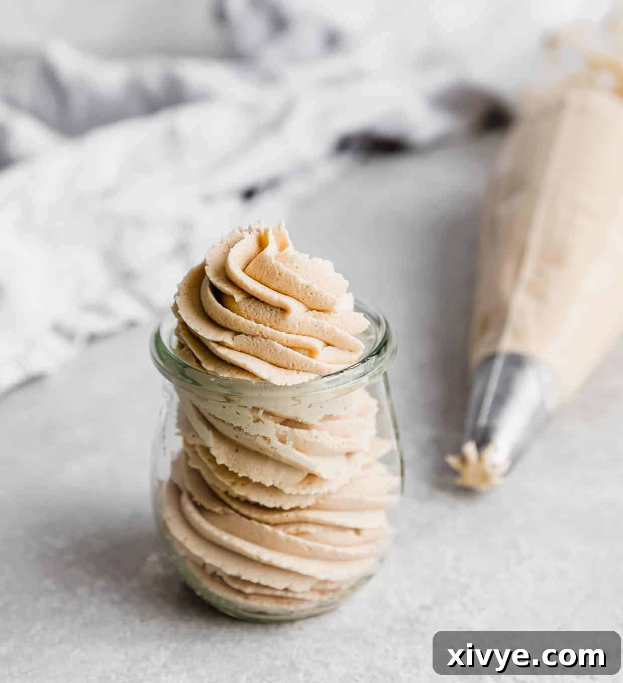 Peanut Butter Frosting piped into a small glass jar on a white background.