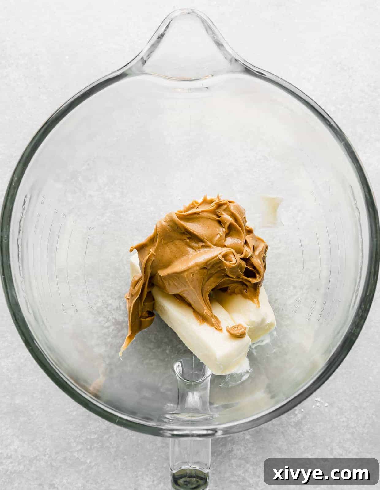 A glass stand mixer bowl with butter and peanut butter in it.