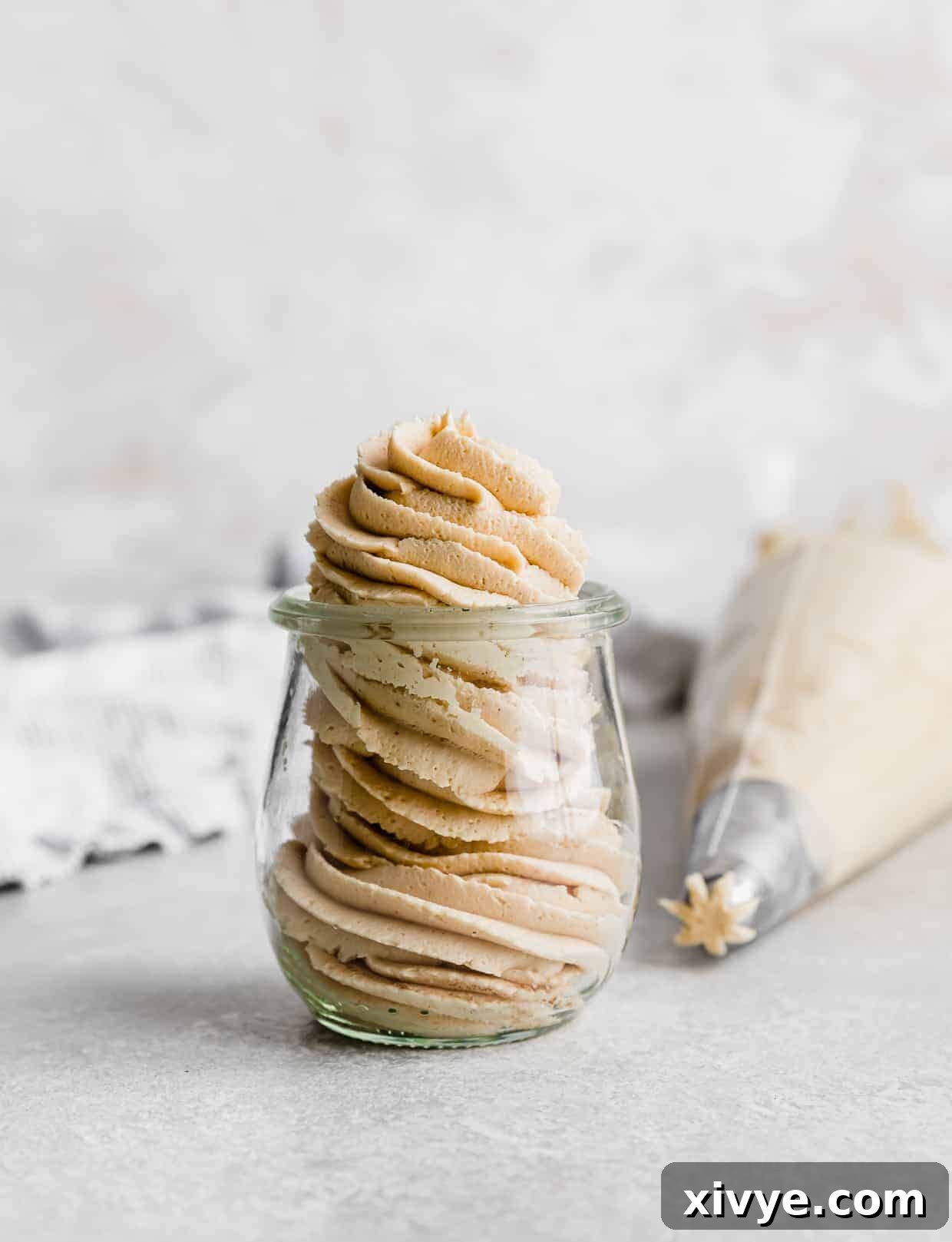 A glass jar with Peanut Butter Frosting piped into the jar using a swirly tip.