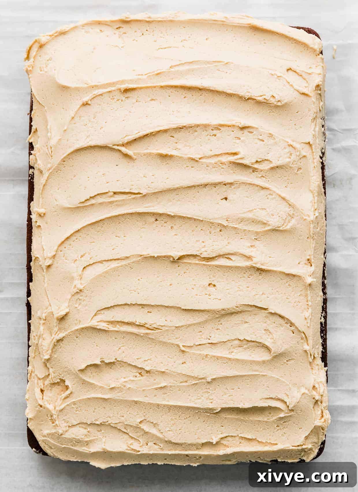 A light golden colored peanut butter frosting spread across a sheet chocolate cake.