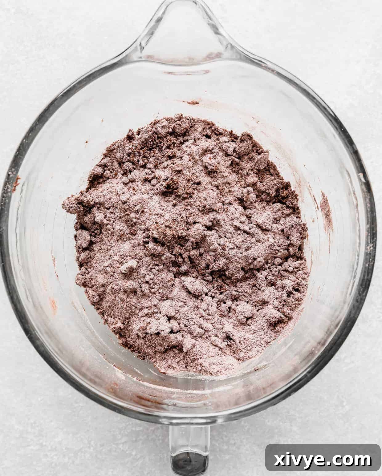 A gray brown colored dry ingredient mix in a glass bowl with chunks of butter throughout.