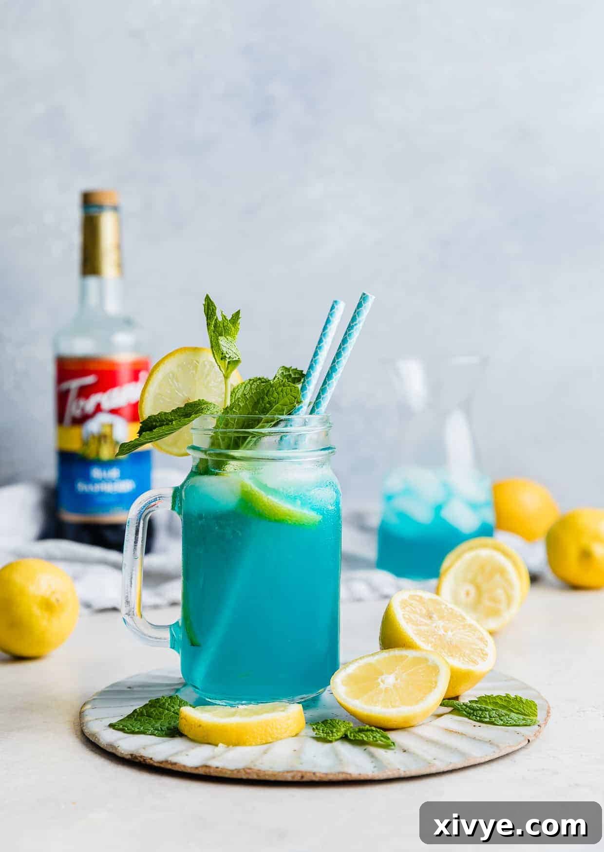 A large glass jar filled with bright blue raspberry lemonade and sliced lemons, set against a blurred background, emphasizing its refreshing appeal.
