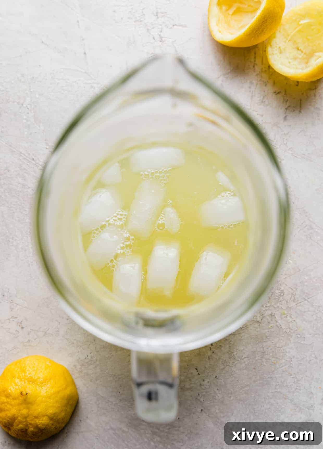 An overhead view of a clear glass pitcher brimming with lemon juice and ice, demonstrating the initial mixture before adding flavor.