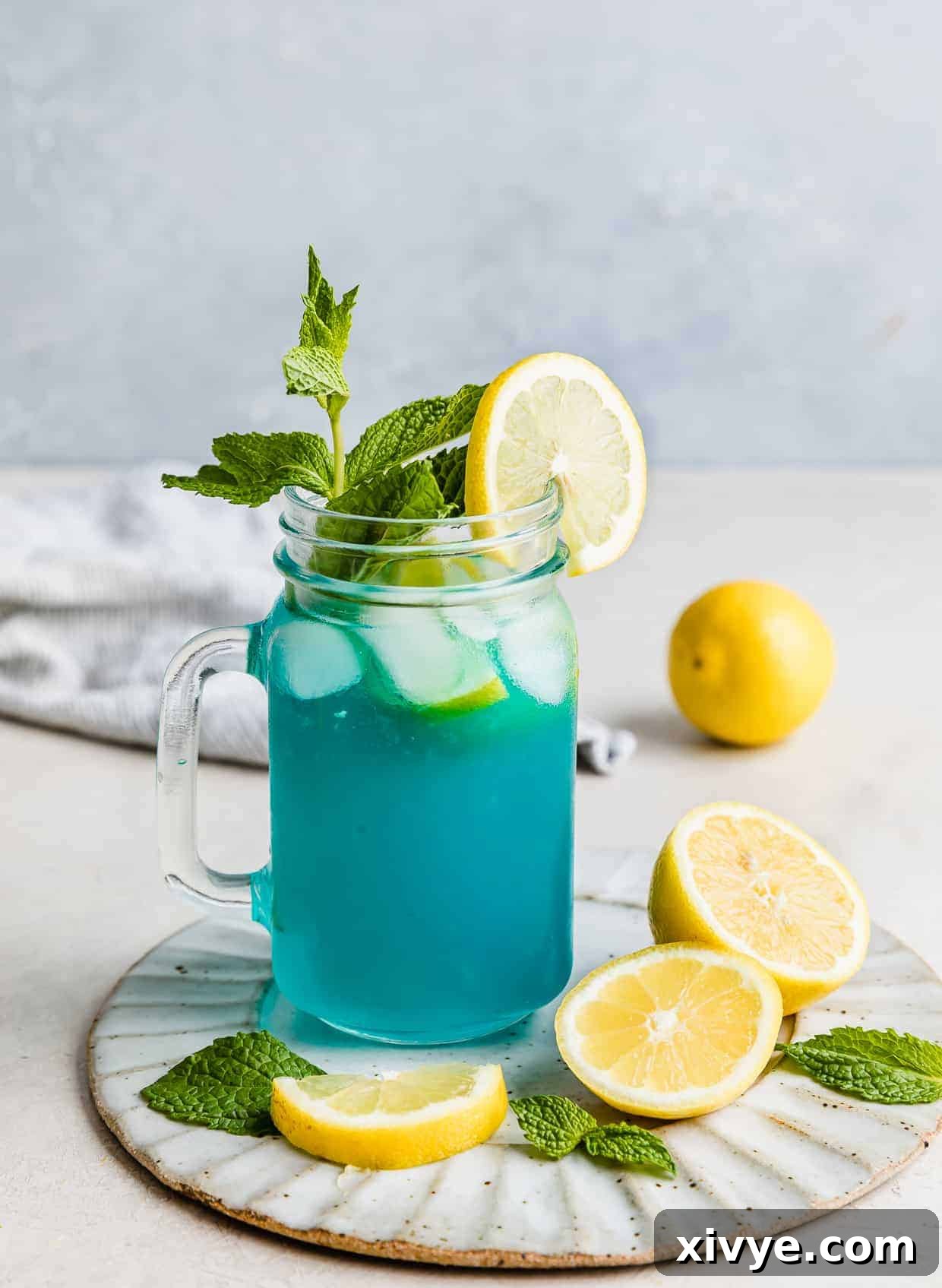 A glass jar of blue raspberry lemonade, beautifully garnished with a sprig of fresh mint, inviting a refreshing sip.