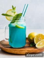 A jar of Blue Raspberry Lemonade on a brown plate, garnished with a sprig of fresh mint and lemon slice.