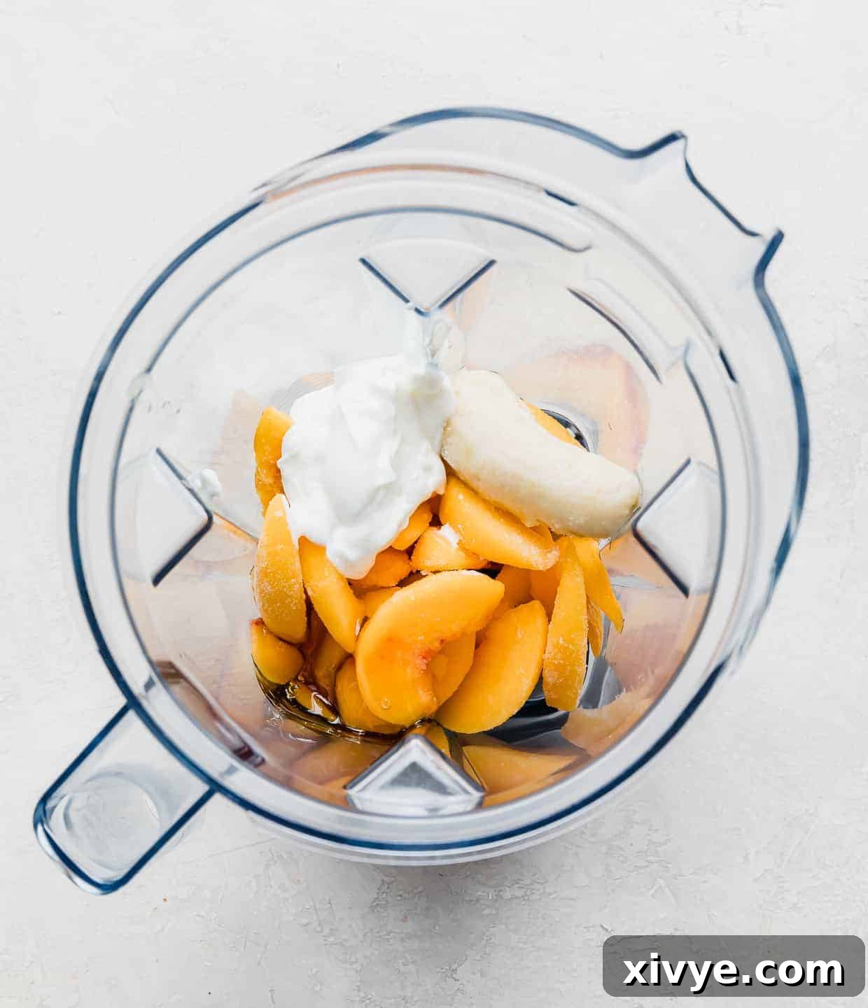 Overhead photo of a blender filled with frozen peach slices, yogurt, banana, milk, and honey.