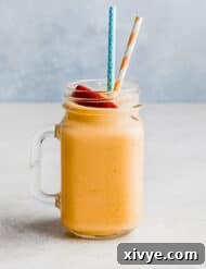 A glass cup filled with a banana peach smoothie mixture and two straws.