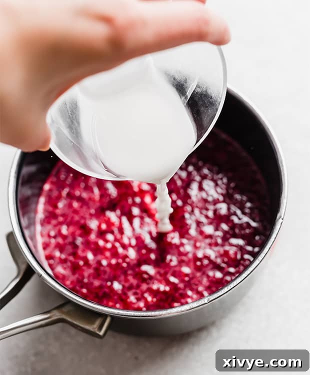 A cornstarch slurry being poured into a saucepan full of a raspberry compote.