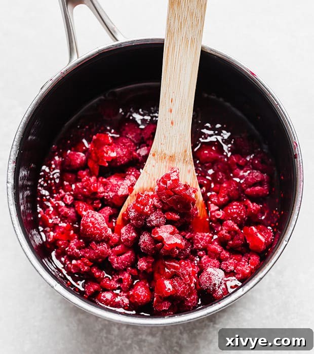 Raspberry sauce in a saucepan with a wooden spoon scooping some up.