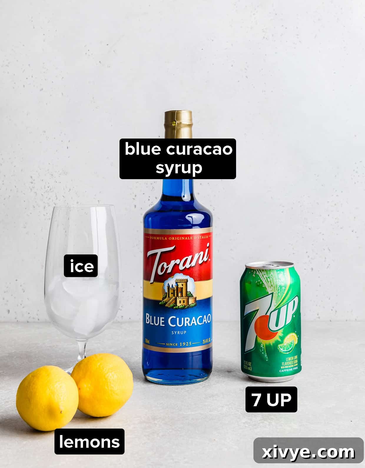 Tropical Azure Cooler 4 A flat lay of ingredients used to make a virgin blue lagoon drink recipe, including blue curacao syrup, 7UP, and fresh lemons.