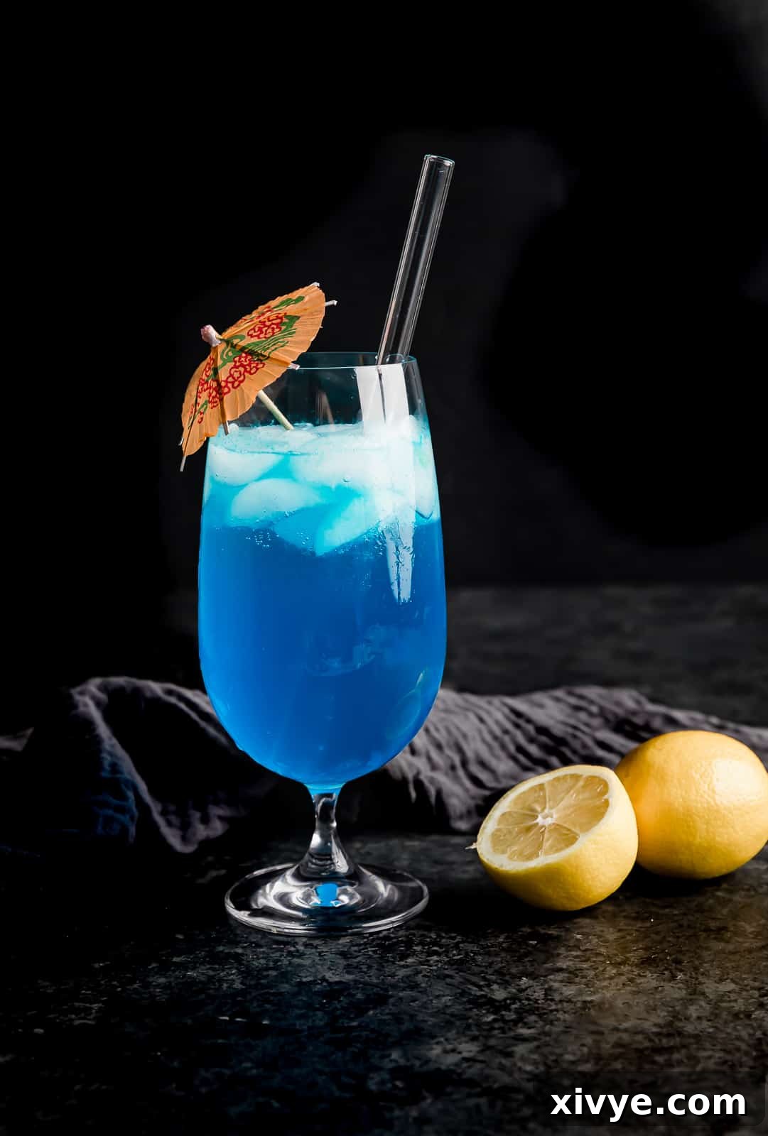 Tropical Azure Cooler 6 A glass cup full of a blue lagoon drink with a pink umbrella in the cup, ready to be enjoyed.
