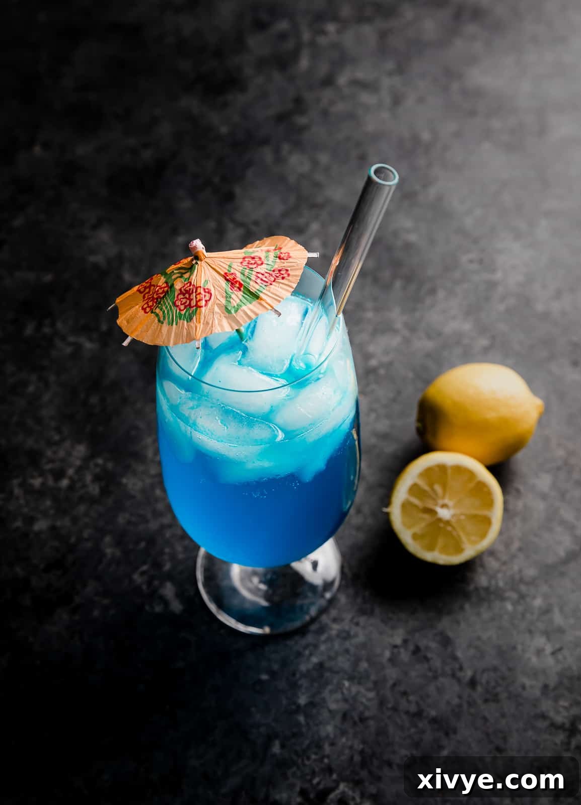 Tropical Azure Cooler 7 A Blue Lagoon Mocktail on a black background with a fresh lemon next to the glass, highlighting its striking color.