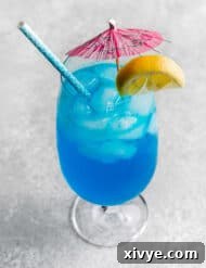 A Blue Lagoon Mocktail in a large glass cup with a pink umbrella and lemon slice on the rim.