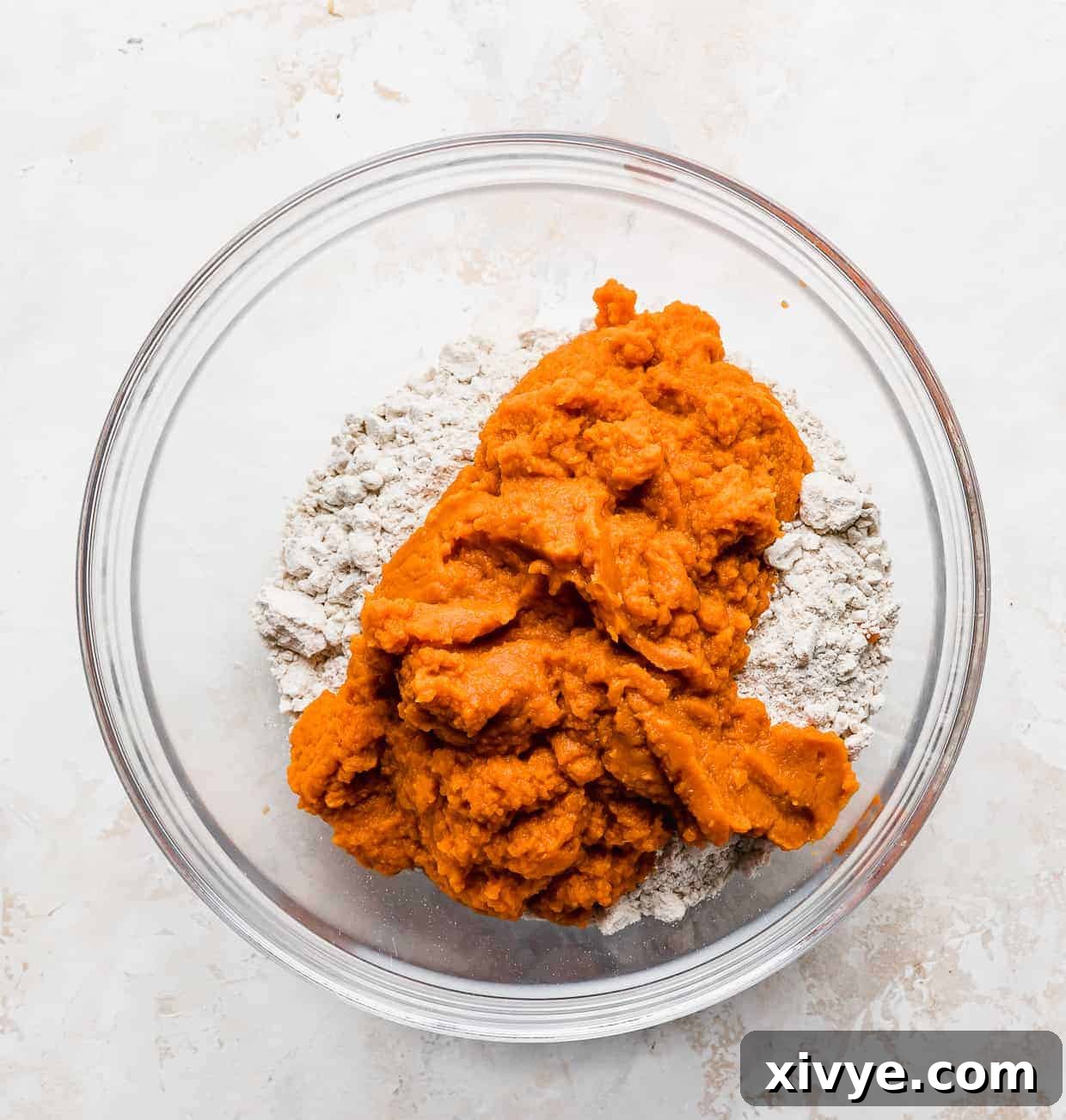 A cake mix and pumpkin puree in a glass bowl, ready to be mixed for delicious muffins.