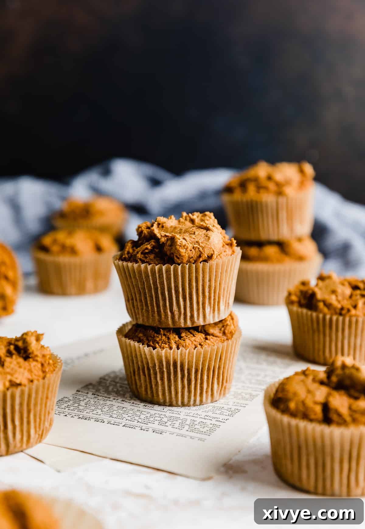 Two pumpkin muffins stack on top of each other against a brown background, showcasing their golden crumb.