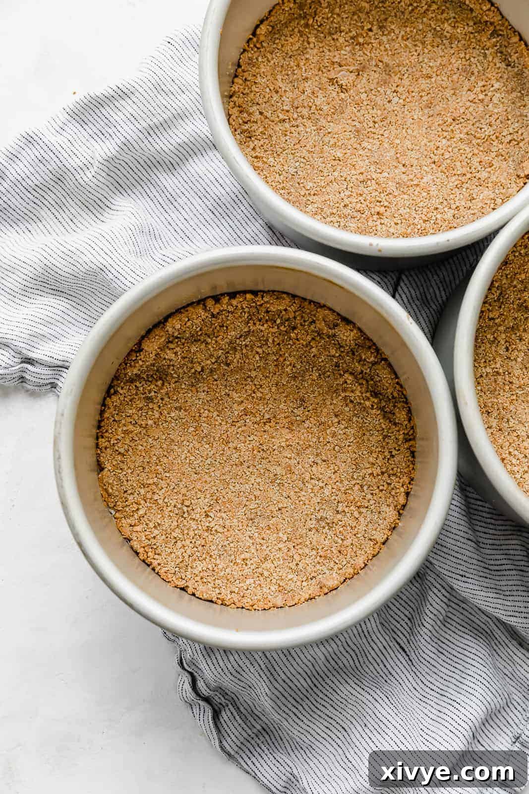 A golden-brown graham cracker crust neatly pressed into the bottom of a 6-inch round cake pan, ready for the cake batter.