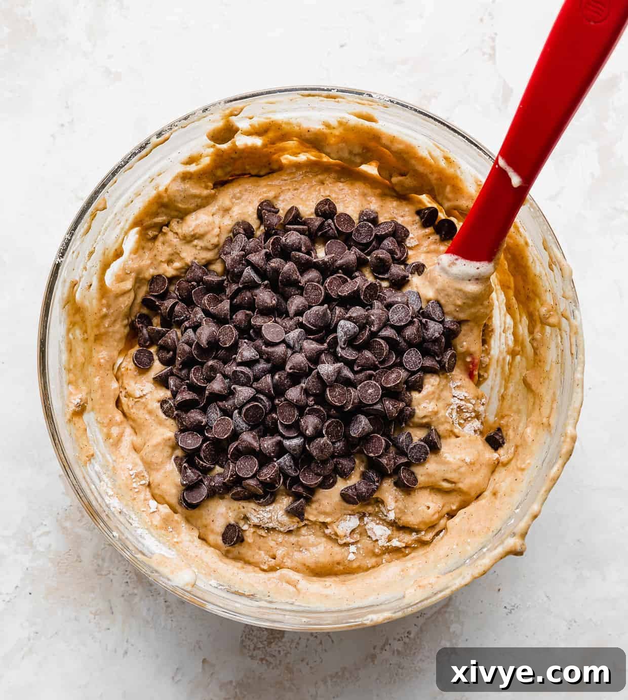 An abundance of chocolate chips generously scattered over the vibrant orange pumpkin pancake batter, ready to be gently folded in to create delicious pockets of melted chocolate.