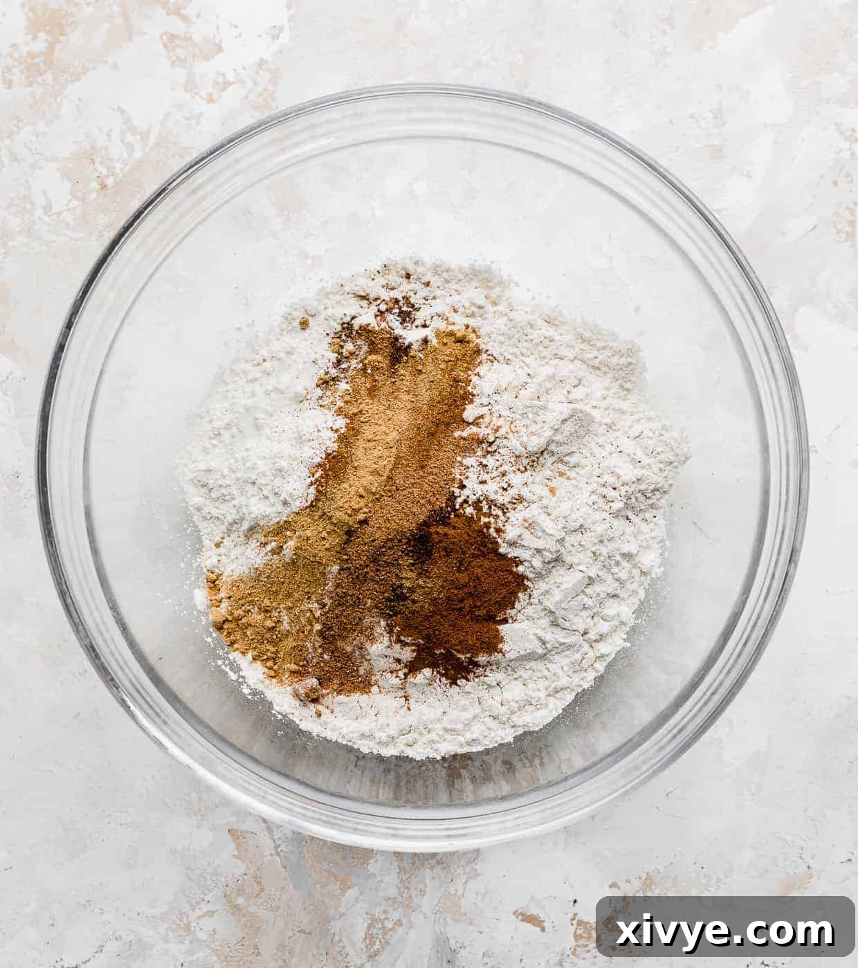 A glass bowl filled with the precisely measured dry ingredients for Fluffy Pumpkin Chocolate Chip Pancakes, including flour and a blend of fall spices, ready for whisking.